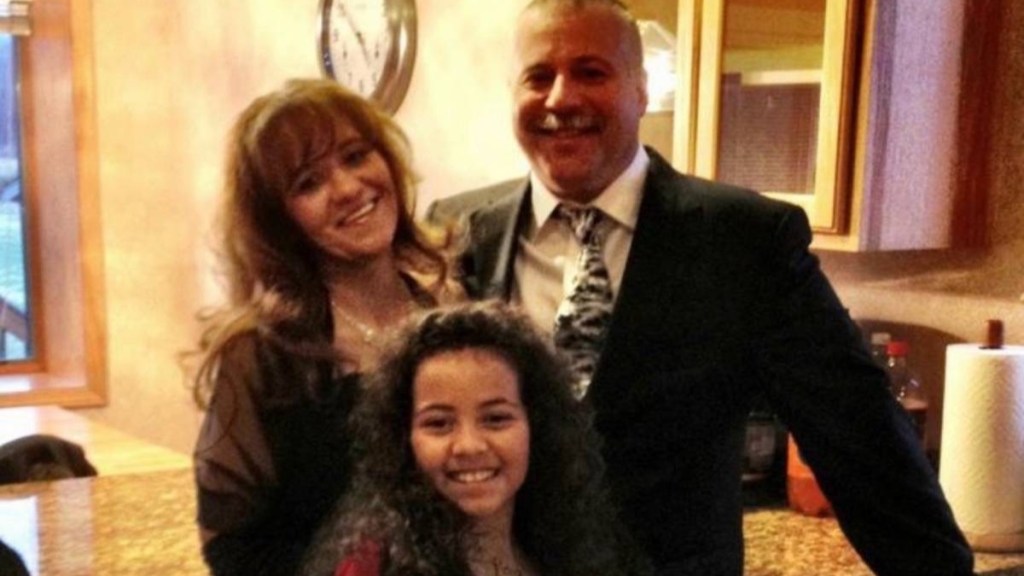 An old photo of Lauren Campbell and her parents from when she was a kid. Mom, Dad, and Lauren smile as they pose together in a kitchen.