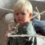 Close up of a toddler as he holds a decorative Halloween skeleton close. The toddler has a serious expression on his face as he gazes into the camera