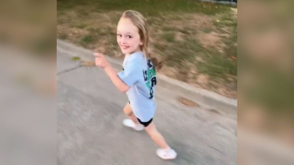 A little girl running down the block and smiling.