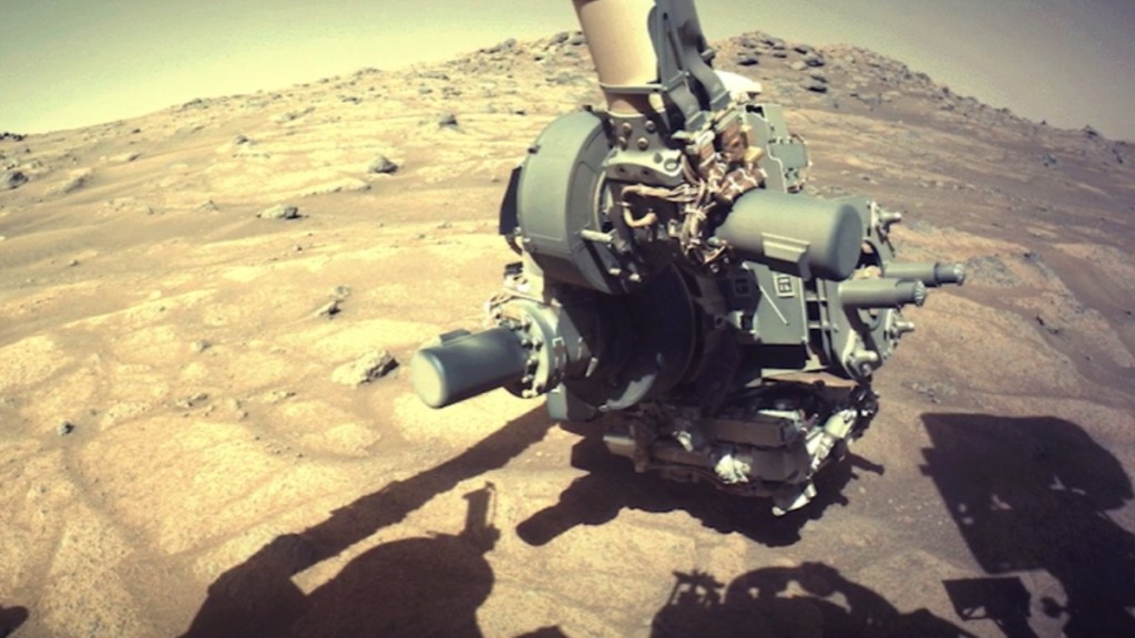 Footage from Mars. A giant machine can be seen, as well as its shadows. The rocky planet surface can also be seen at a good distance behind the machine