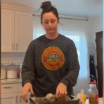 A woman looks down, blank look on her face, as she gathers items on the kitchen counter