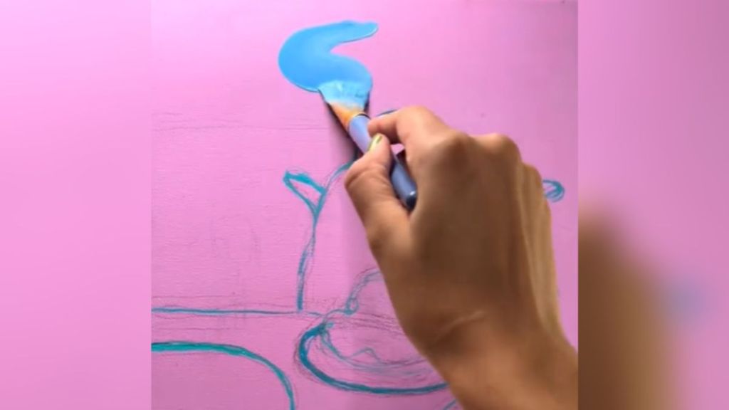 A woman painting a blue stripe onto a pink canvas.