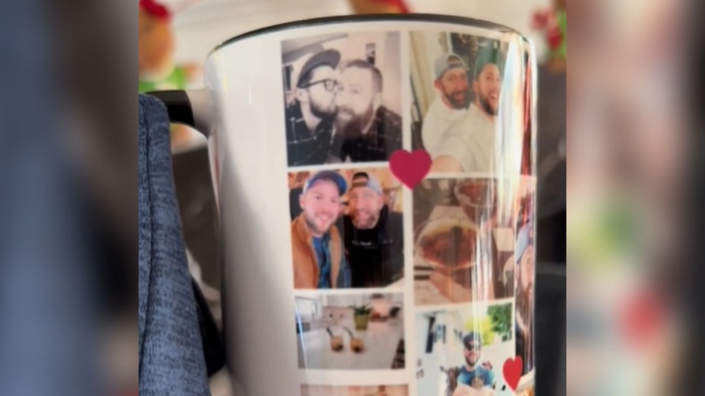 Close up of a mug being held by someone. The mug has various images of two men. The mug has red hearts throughout.