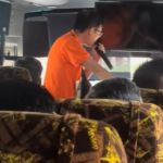 A tour guide in an orange shirt using a microphone.