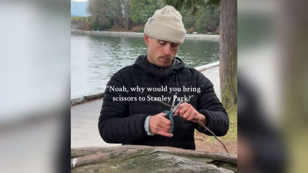 A man in the park cutting a stick with scissors.