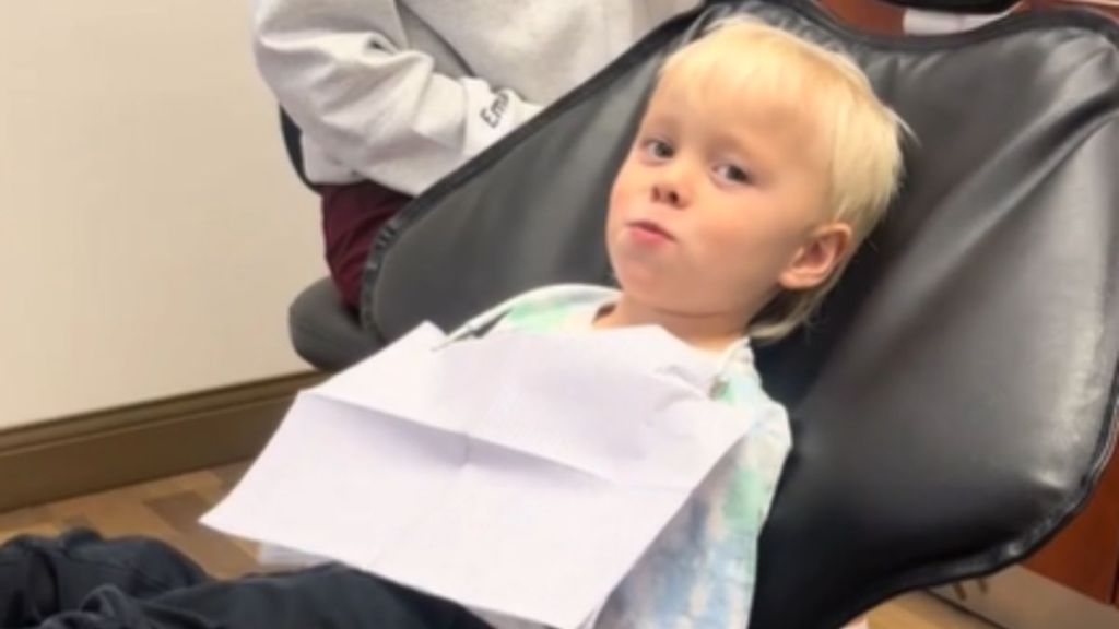 A little boy sitting in the dentist's chair with a sly smile.