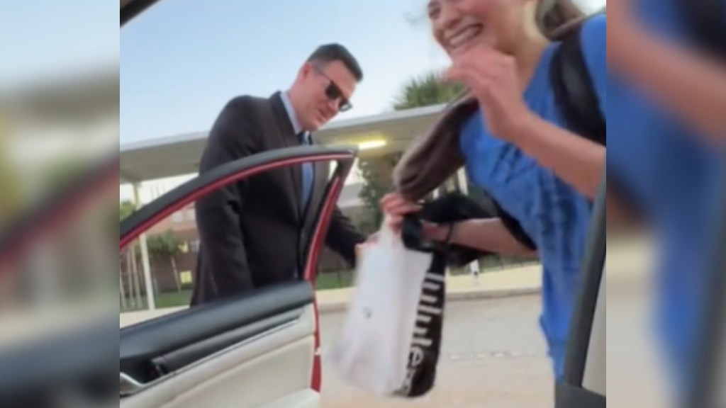 View from inside a car. A man in a suit opens the car door, smiling. He's also wearing sunglasses. He opens the door for a little girl who is smiling wide as she laughs.