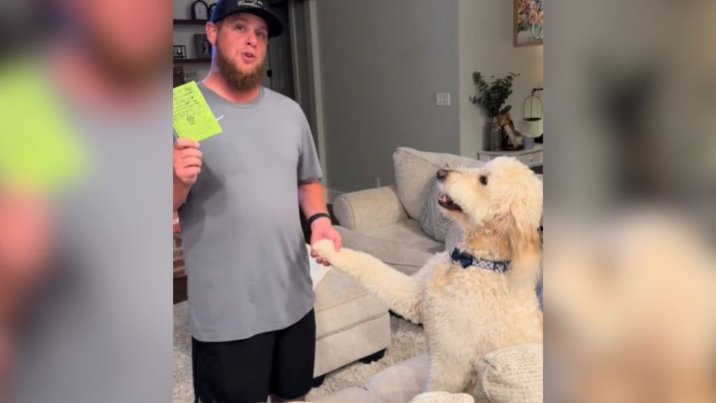 A man holding his dog's paw in one hand and a piece of paper in the other.