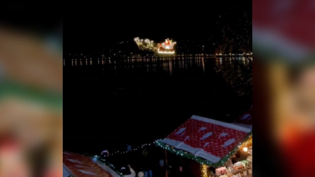 Distant view of Santa flying pas in a sleigh in the sky above festive buildings