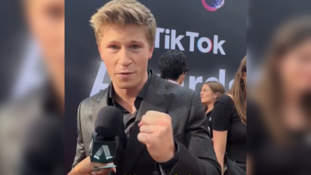 Robert Irwin looks into the camera as he talks into a mic on a red carpet. He has a hand in a fist as he talks passionately