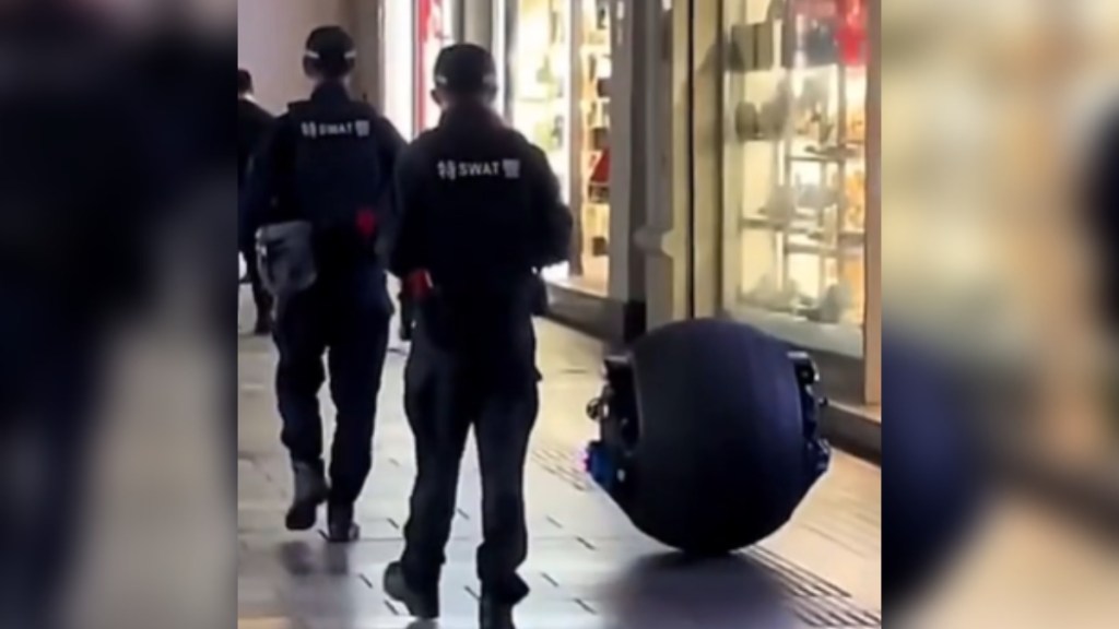 View from behind of two police officers in China as the walk alongside a spherical robot