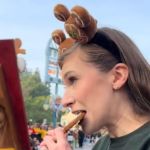 A woman takes a bite of a gingerbread cookie as a horrified giant gingerbread man looks on.