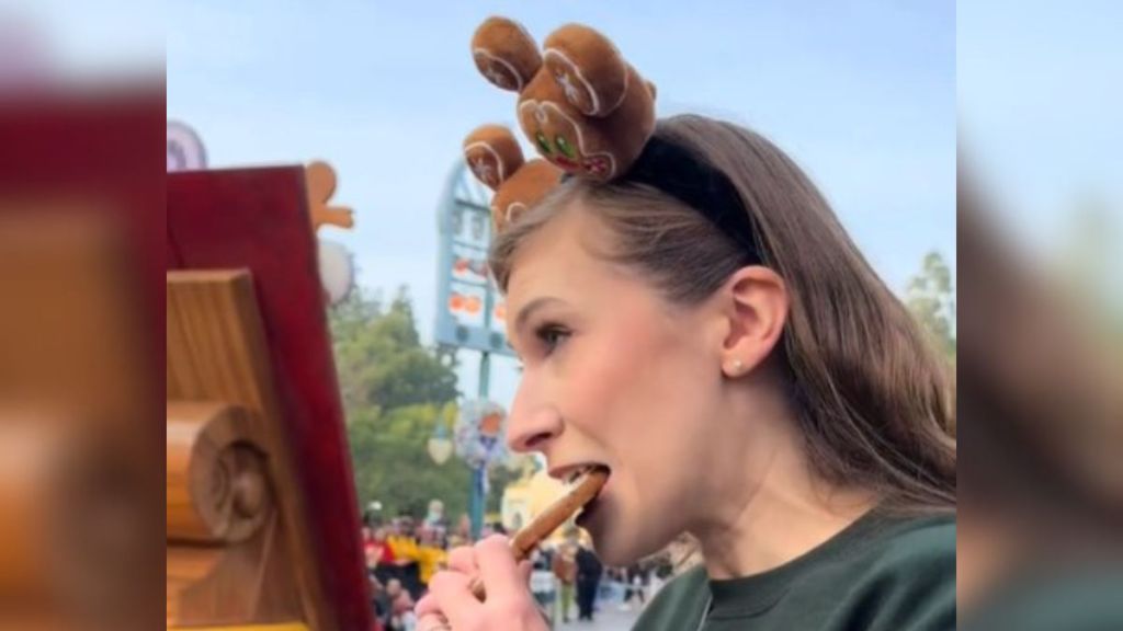 A woman takes a bite of a gingerbread cookie as a horrified giant gingerbread man looks on.