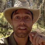 Close up of a man talking passionately to a camera. He stands outside in a forest area, monarch butterflies flying all around in the distance