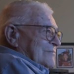 Close up of an elderly man sitting in a living room. He smiles as he looks at something not shown in this image