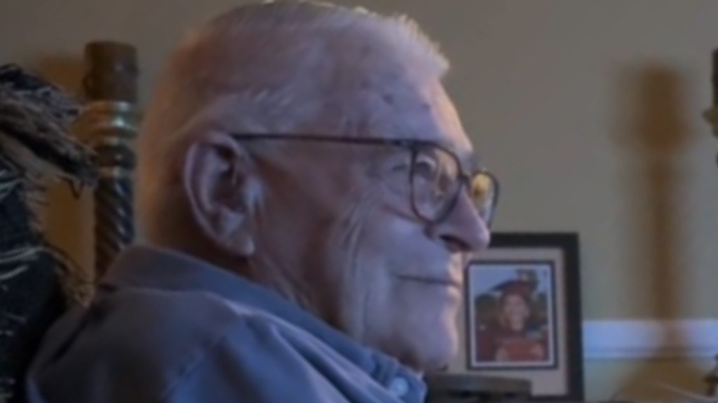 Close up of an elderly man sitting in a living room. He smiles as he looks at something not shown in this image