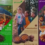 Close up of three boxes of Girl Scout cookies: Thin Mints, adventurefuls, and samoas