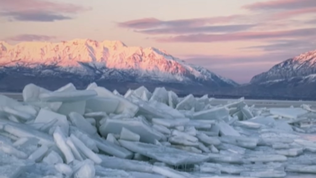 A large pile of ice shoves rests at Utah Lake. In the distance there's a massive snow-covered mountain