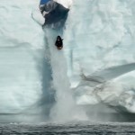 Distant view of a large ice waterfall with a kayaker plummeting over the edge.