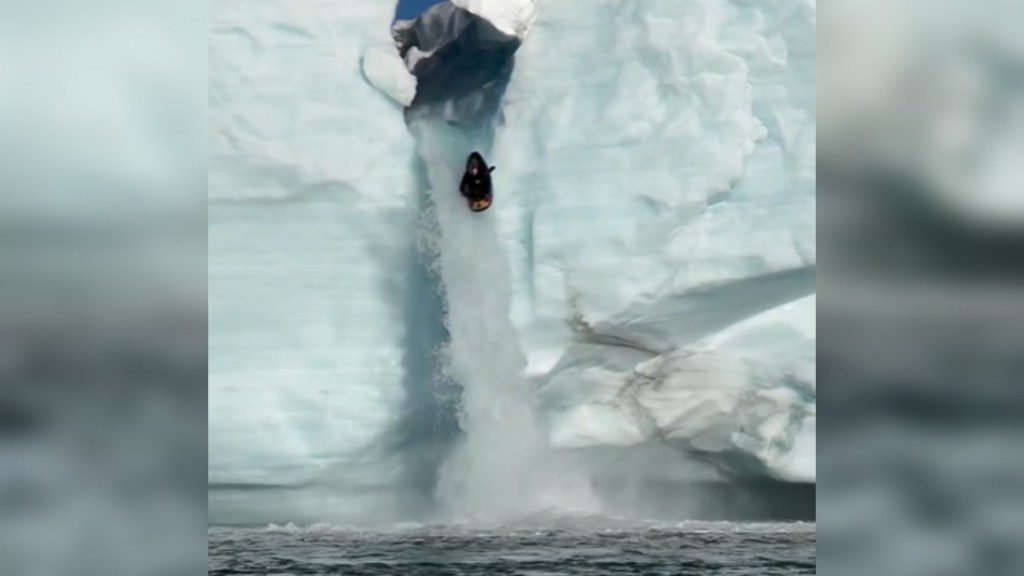 Distant view of a large ice waterfall with a kayaker plummeting over the edge.