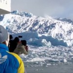 Passengers on a boat lean over to watch the massive iceberg in the distance