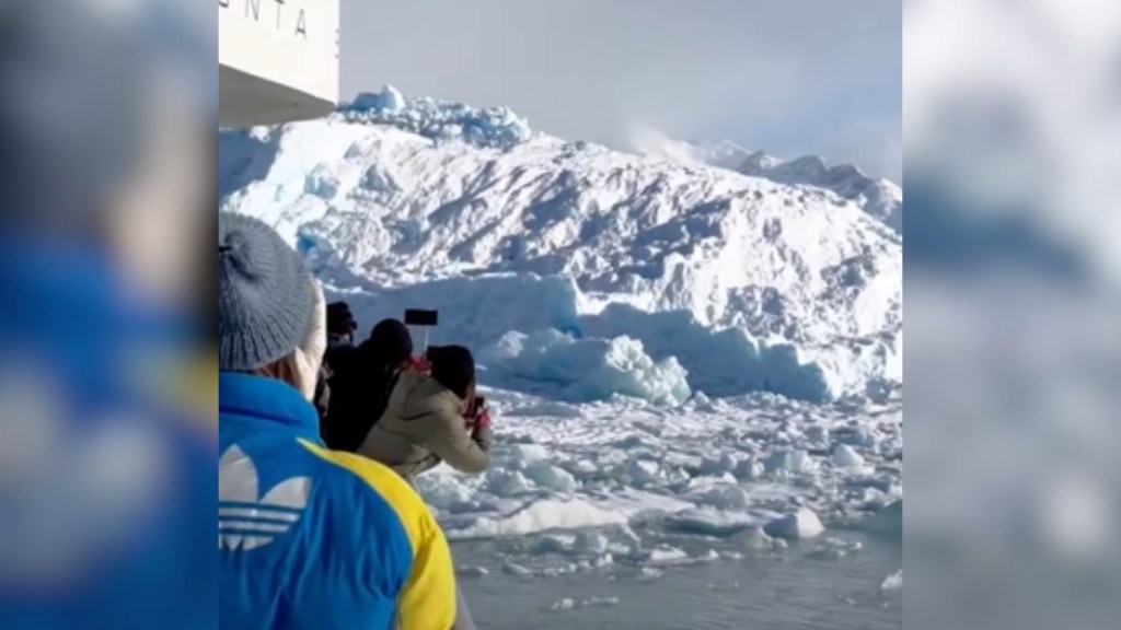 Passengers on a boat lean over to watch the massive iceberg in the distance