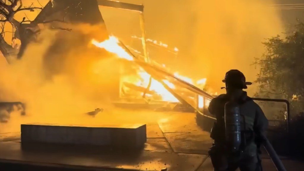 View from behind of a firefighter working to put out a fire that has destroyed a building