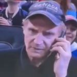 Liam Neeson talking on the phone with an angry expression.