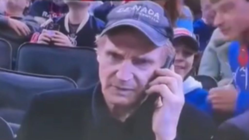 Liam Neeson talking on the phone with an angry expression.