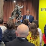 A crowd watches on as a man speaks at a podium in front of a newly unveiled dinosaur specimen at the American Museum of Natural History