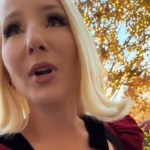 Close up of a blonde woman as she walks and talks outside. She has a shocked look on her face as she looks in the distance at something that can't be seen in this image