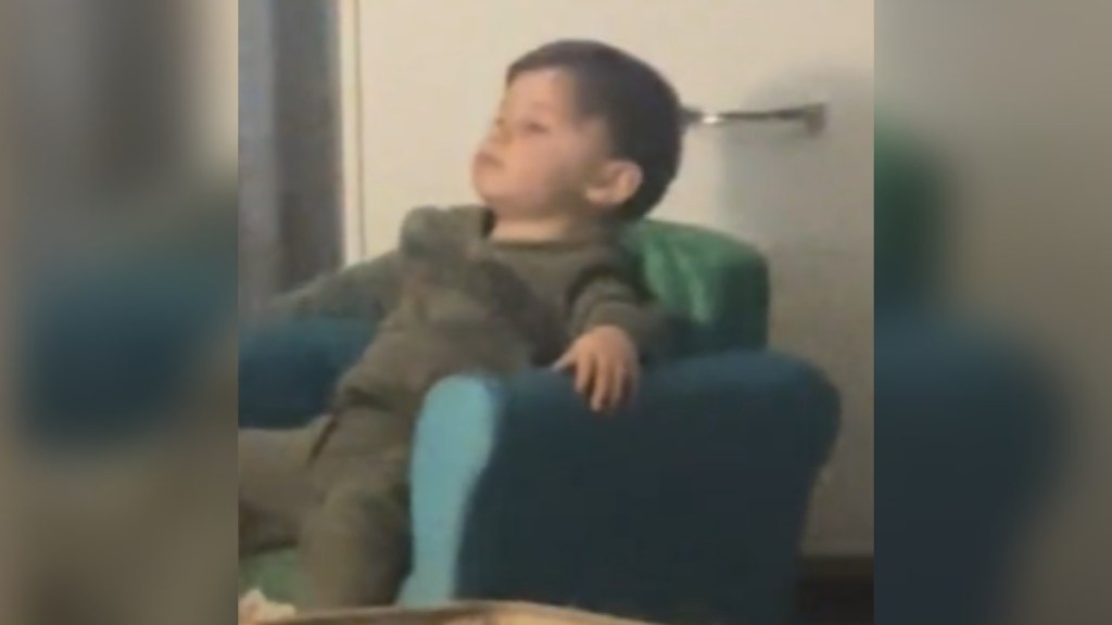 A toddler sits in a kid-sized arm chair. He looks like he's in a daze as he stares into the distance