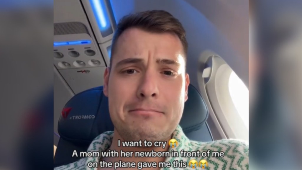 Close up of a man sat inside a plane. He looks emotional, mouth slightly turned down. Text on the image reads: I want to cry. A mom with her newborn in front of me on the plane gave me this