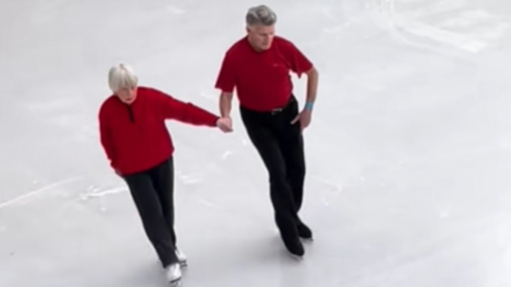 An elderly woman and man hold hands as they skate together on ice