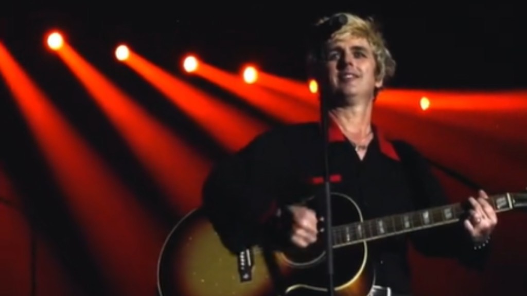 Close up of Billie Joe Armstrong performing onstage. He smiles as he plays a guitar