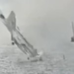 A fighter jet starts to crash, nose first, into water. A nearby fishing vessel can be seen at a distance