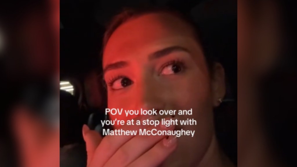 Close up of a woman in a car at night. The glow of a red light lights up her face. She covers her mouth with her hand. She's looking off to the side at something that isn't shown in this image. Text on the image reads: POV you look over and you're at a stop light with Matthew McConaughey