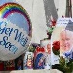 Close up of photos, candles, and a balloon left outside for Pope Francis as he recovers from an illness in the hospital. The balloon says "get well soon" and has a rainbow on it