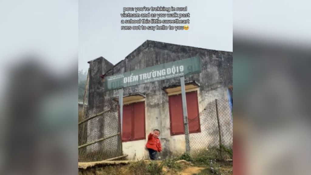 A little boy waving outside a school in Vietnam.