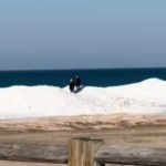 View from a distance of shelf ice that formed on Lake Michigan. Two people stand on the shelf ice, walking around