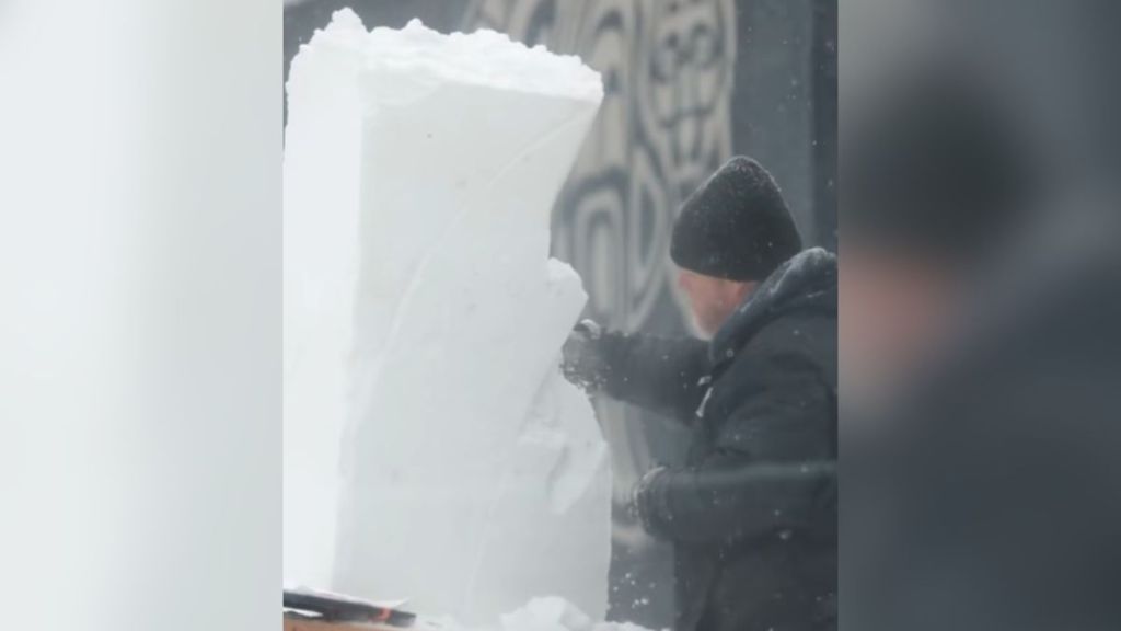 A man carving a sculpture out of snow.