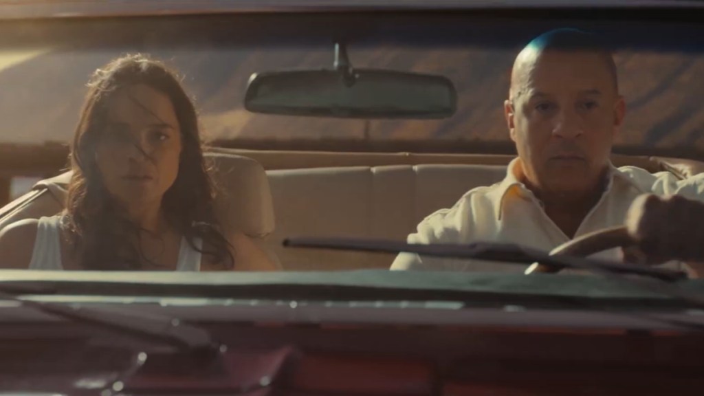 Michelle Rodriguez and Vin Diesel sit in a car. She's in the passenger seat and he's driving. They both look concerned and focused