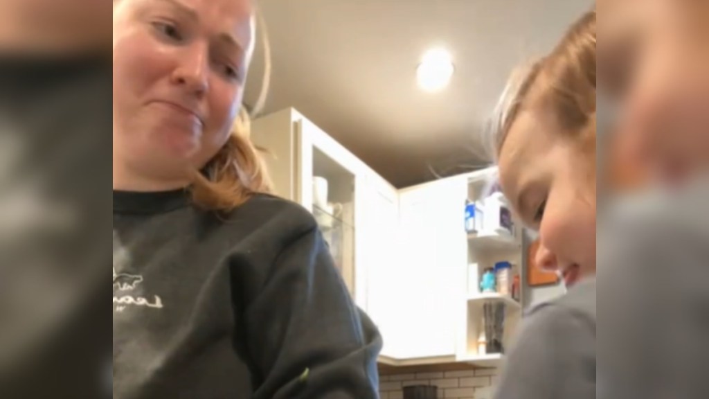 Close up of a mom looking emotional. She's looking lovingly at her toddler who is right next to her at the kitchen counter, smiling as she looks down