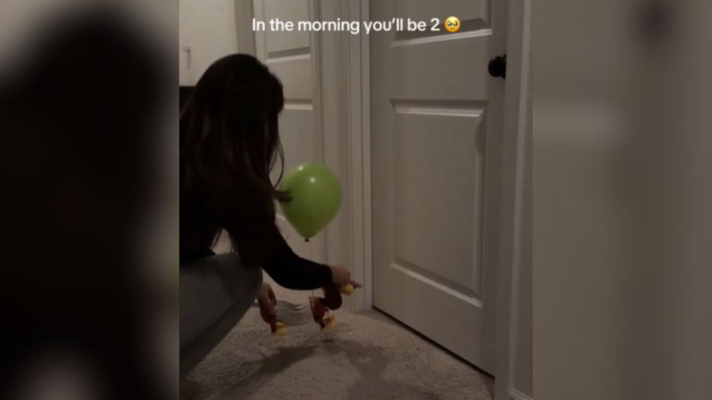 A woman placing a toy with a balloon tied to it in front of a door.