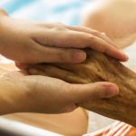 Image shows a family member holding the hand of a patient during Alzheimer's treatment.