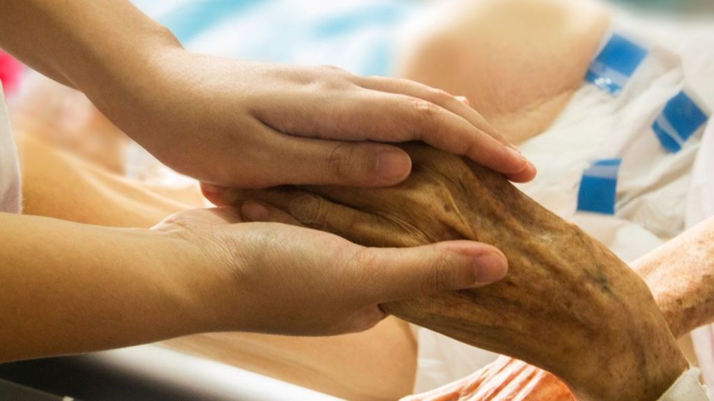 Image shows a family member holding the hand of a patient during Alzheimer's treatment.