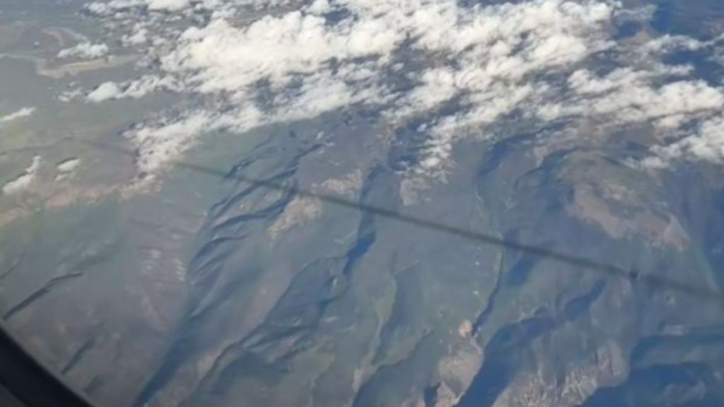 Image shows contrail shadow stretching across the land as seen from an airplane.