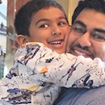 Close up of a man holding a little boy in his arms. They're holding onto each other tightly as they smile wide