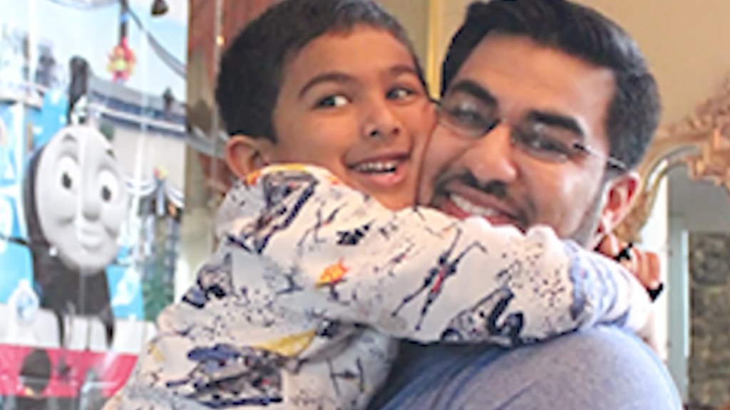 Close up of a man holding a little boy in his arms. They're holding onto each other tightly as they smile wide