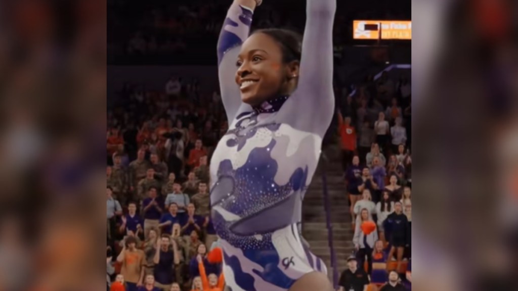 Brie Clark poses, arms in the air, after pulling off the Biles I. She smiles wide.